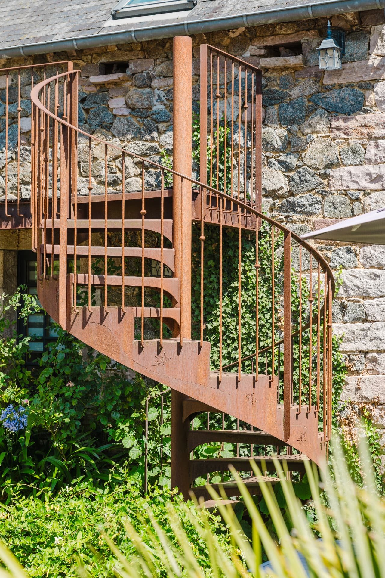 Escalier hélicoïdal en acier patiné adossé au mur de pierre