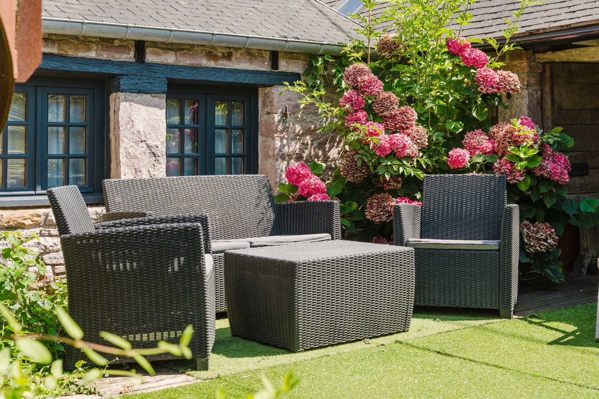 Fauteuils de jardin et hortensias devant les fenêtres bleues de la maison en pierre