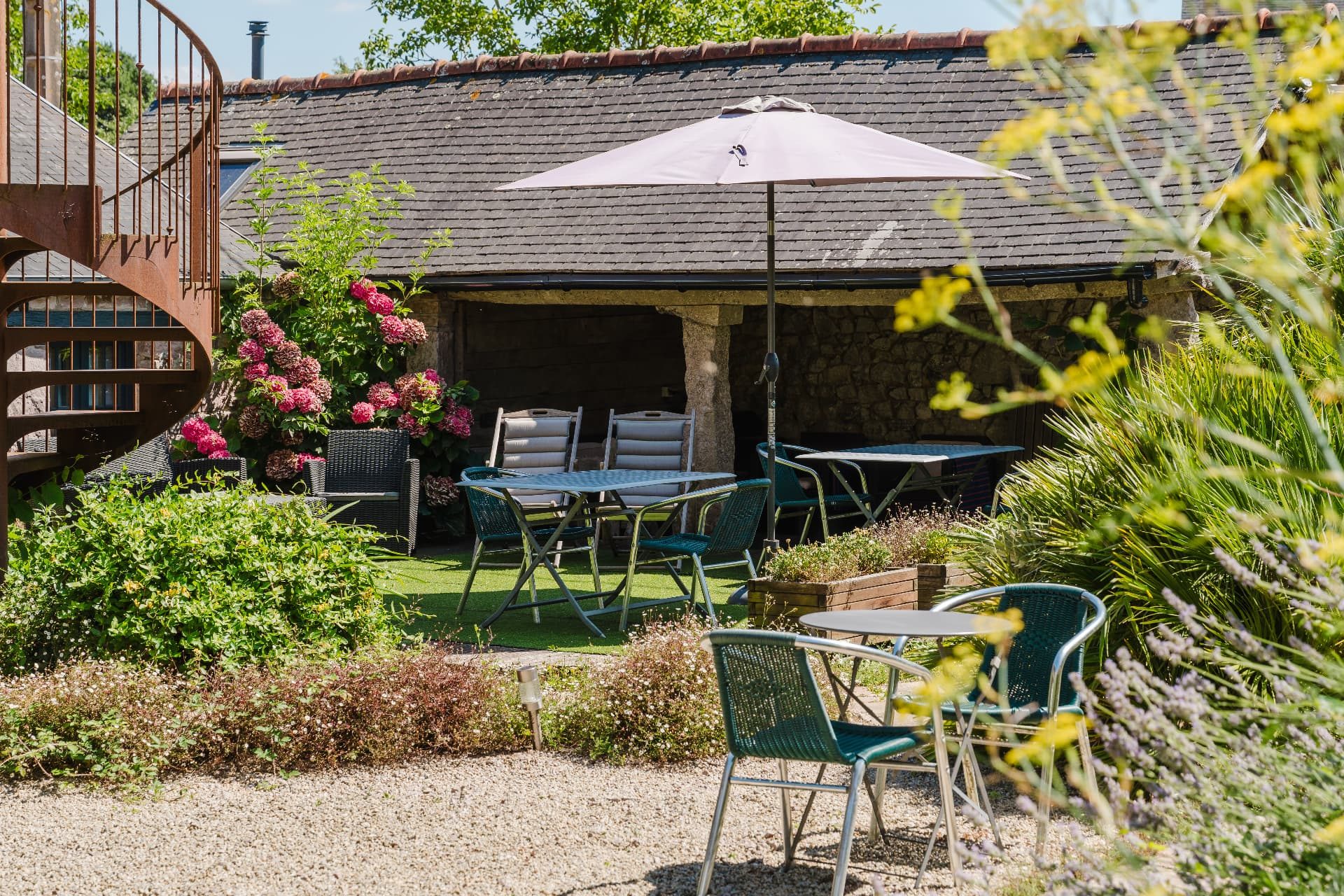 Cour fleurie du Relais Saint-Aubin avec tables, parasol et massifs d'hortensias