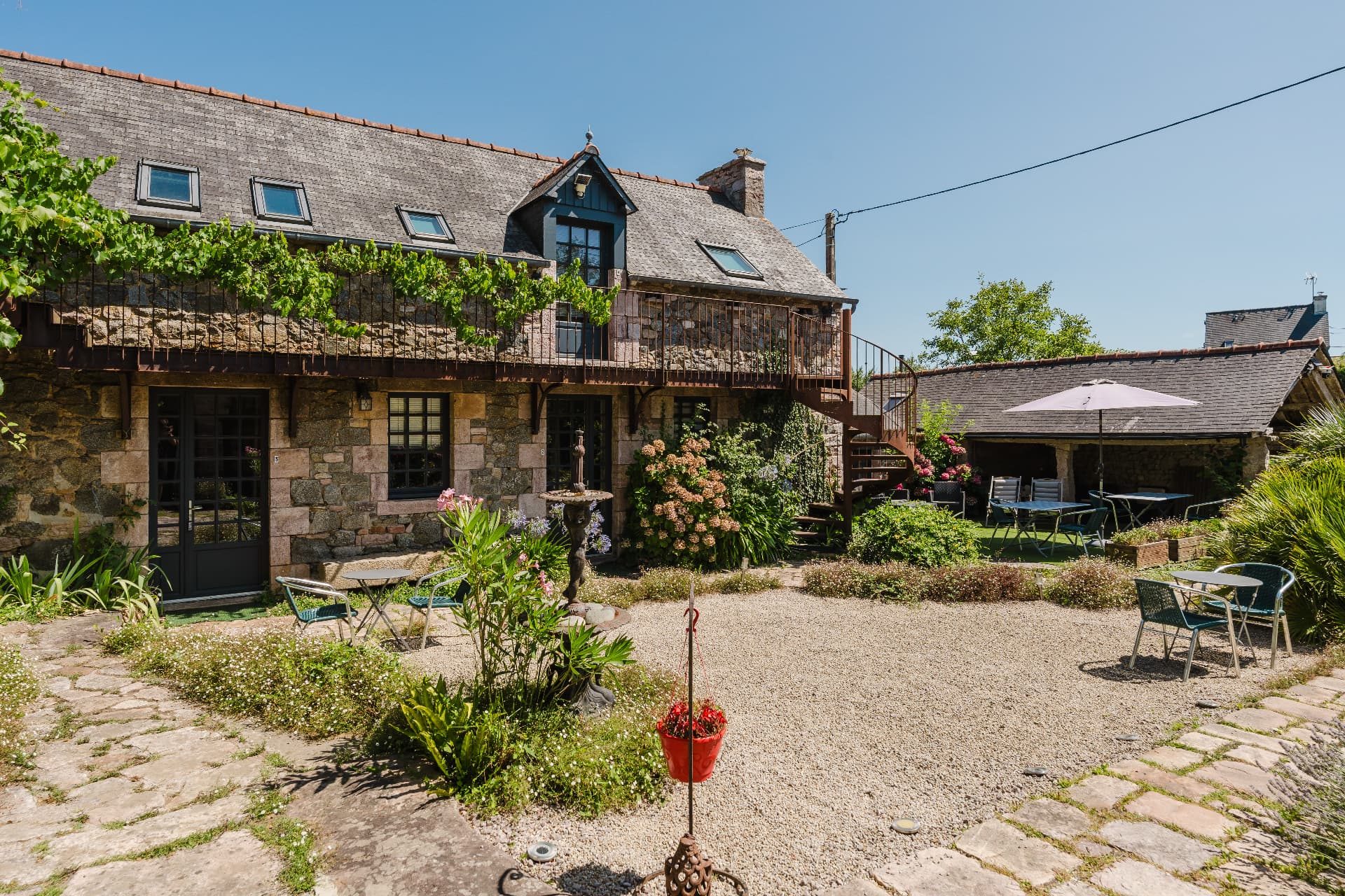 La cour gravillonnée du Relais Saint-Aubin avec ses tables et son parasol en été